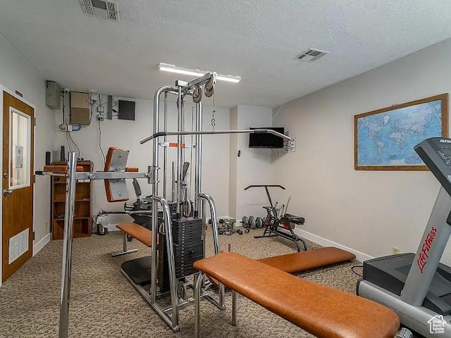 exercise room with carpet floors, visible vents, and a textured ceiling