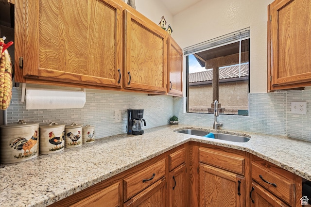 kitchen with brown cabinetry, a sink, backsplash, and light stone countertops