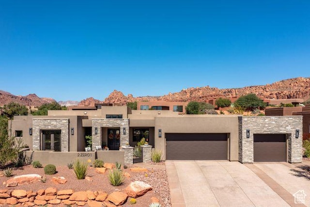 view of front facade featuring a garage, concrete driveway, stone siding, a mountain view, and stucco siding