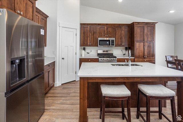 kitchen with wood finished floors, a sink, vaulted ceiling, and stainless steel appliances