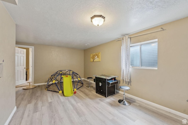 recreation room with a textured ceiling, wood finished floors, and baseboards