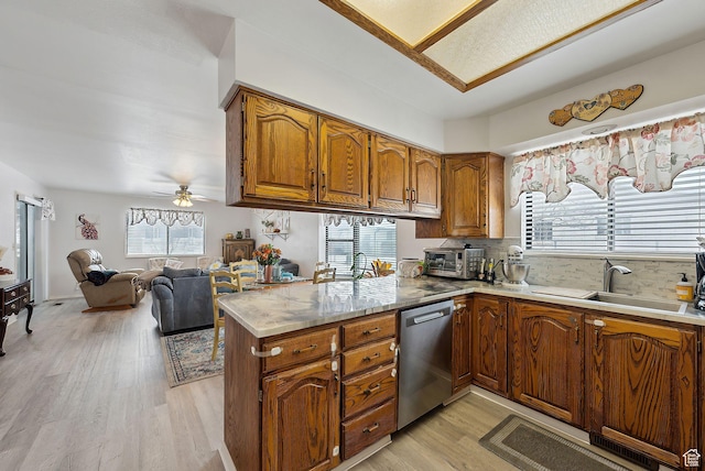 kitchen with brown cabinetry, open floor plan, a peninsula, stainless steel dishwasher, and a sink