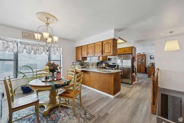 kitchen with appliances with stainless steel finishes, a chandelier, light wood-style floors, a peninsula, and brown cabinetry
