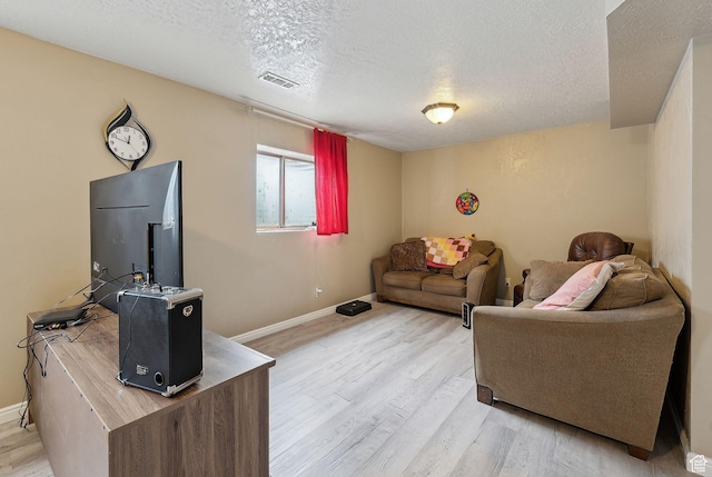 living room with a textured ceiling, visible vents, baseboards, and light wood-style floors