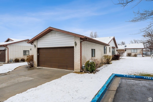 view of snow covered exterior featuring concrete driveway and brick siding