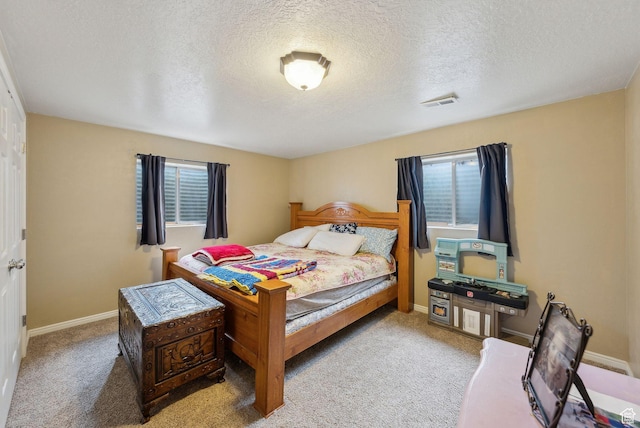 carpeted bedroom featuring a textured ceiling, multiple windows, and visible vents