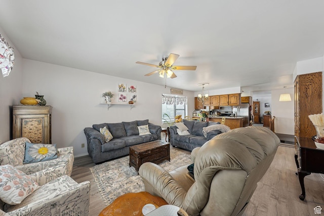 living area with baseboards, light wood-type flooring, and ceiling fan with notable chandelier