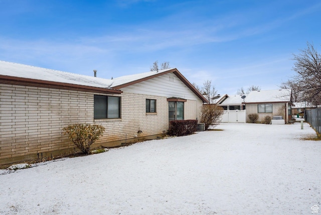 snow covered property featuring cooling unit, brick siding, and fence