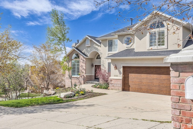view of front of property with concrete driveway, an attached garage, stucco siding, brick siding, and roof with shingles