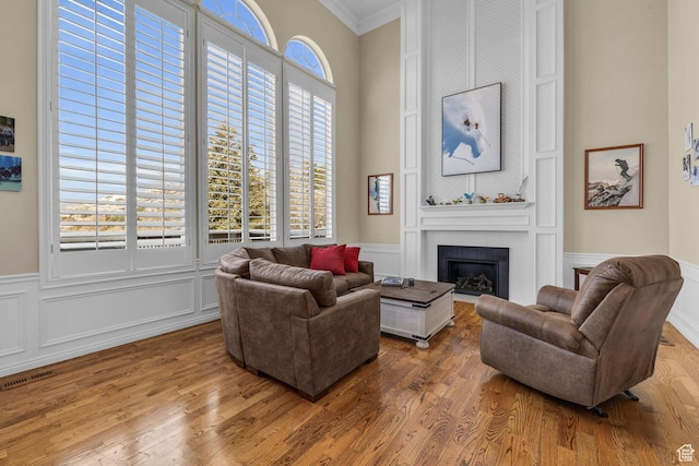living area with wood finished floors, visible vents, a large fireplace, and crown molding