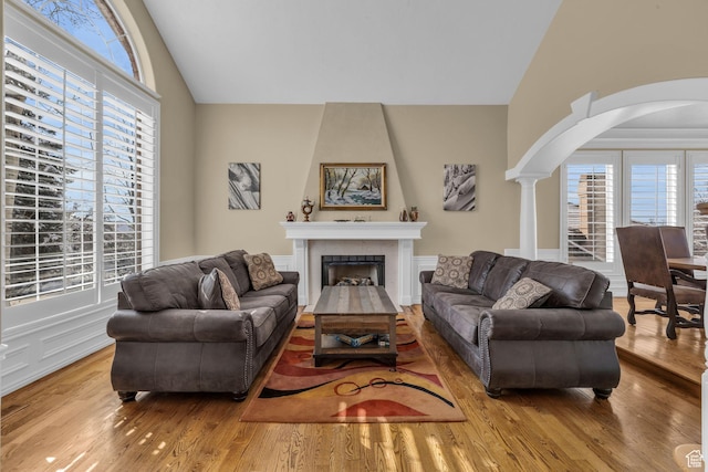 living room featuring high vaulted ceiling, arched walkways, wood finished floors, and a fireplace