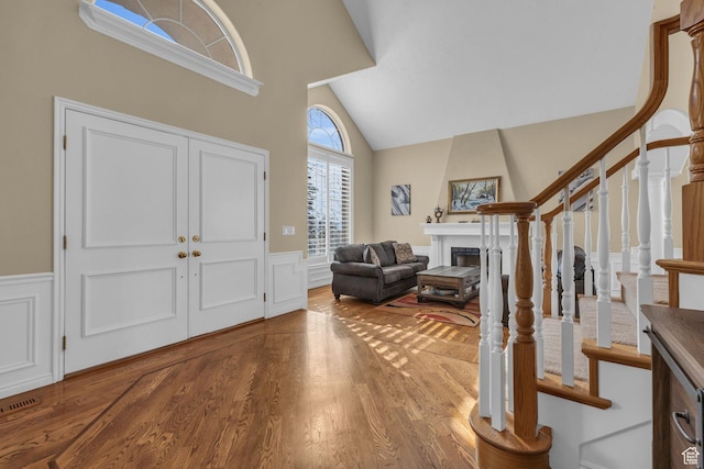 entrance foyer featuring high vaulted ceiling, stairs, wood finished floors, a wainscoted wall, and a large fireplace