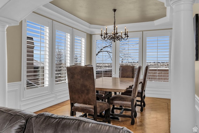 dining room featuring light wood finished floors, ornate columns, a decorative wall, crown molding, and a chandelier