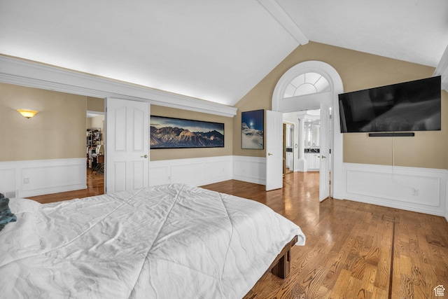 bedroom with lofted ceiling with beams, a wainscoted wall, wood finished floors, and a decorative wall