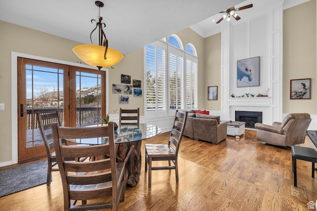 dining area with light wood finished floors, a high ceiling, ceiling fan, a fireplace, and ornamental molding