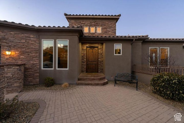 view of exterior entry with stone siding and a patio