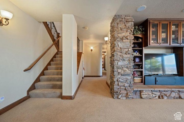 interior space with a textured ceiling, baseboards, stairs, and light colored carpet