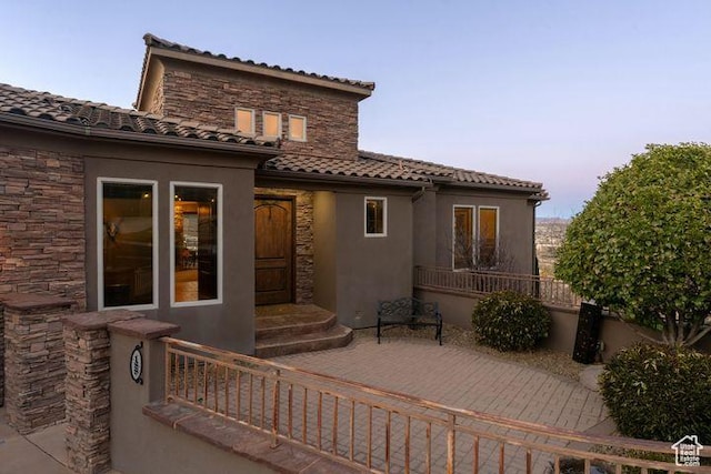 back of property at dusk featuring stone siding, a tile roof, and stucco siding