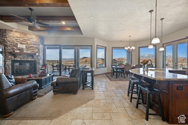living area with baseboards, a textured ceiling, stone tile flooring, a fireplace, and ceiling fan with notable chandelier