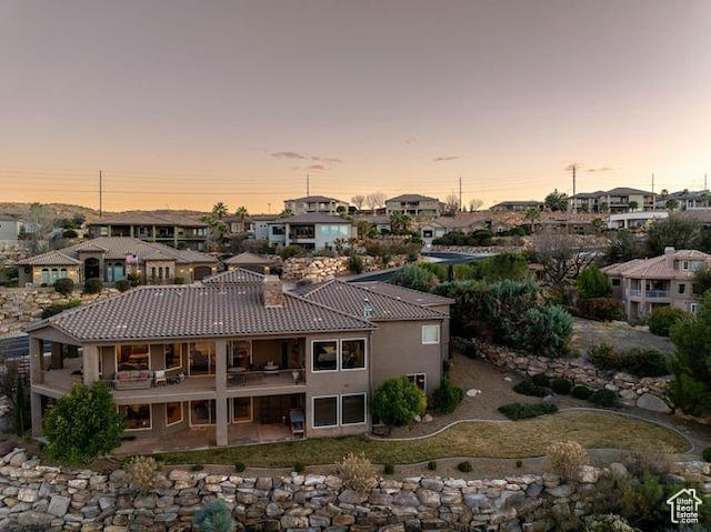 back of property with a tiled roof, a residential view, stucco siding, a chimney, and a patio area