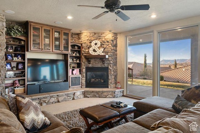 living area with a textured ceiling, a stone fireplace, and a ceiling fan