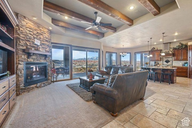 living room with recessed lighting, stone tile flooring, a stone fireplace, beamed ceiling, and ceiling fan with notable chandelier