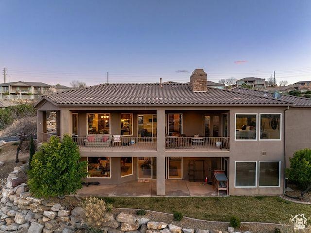 back of house with a patio, a chimney, a tiled roof, and stucco siding