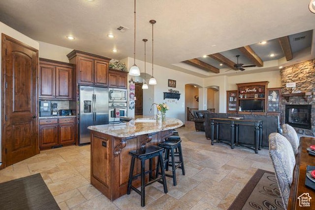 kitchen featuring arched walkways, pendant lighting, appliances with stainless steel finishes, open floor plan, and a large island with sink