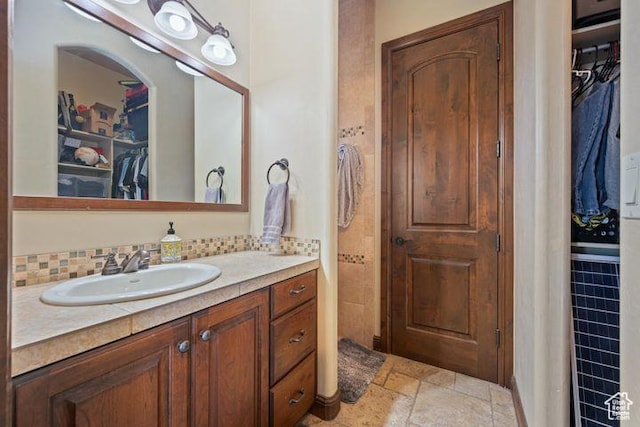 bathroom with tasteful backsplash, stone tile floors, a spacious closet, and vanity
