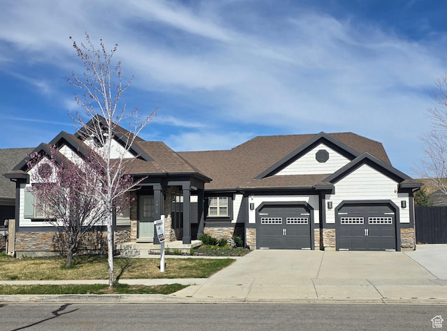 craftsman-style home featuring concrete driveway, stone siding, a garage, and a shingled roof