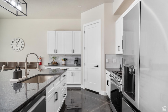 kitchen with tasteful backsplash, appliances with stainless steel finishes, white cabinets, a sink, and dark stone countertops