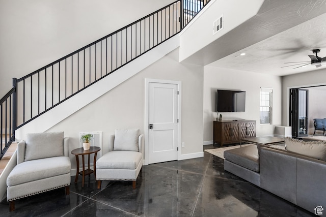 living room with finished concrete flooring, visible vents, a towering ceiling, ceiling fan, and baseboards