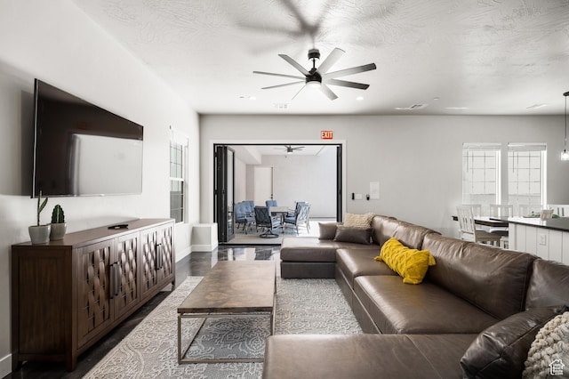 living room with ceiling fan, a textured ceiling, baseboards, and wood finished floors