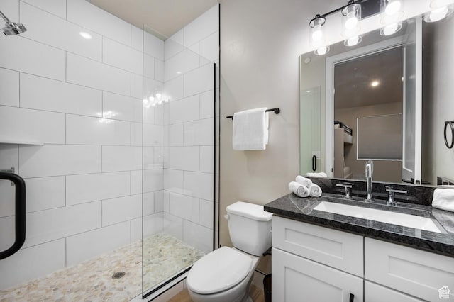 full bathroom with a tile shower, vanity, and toilet