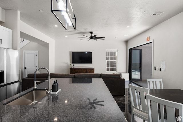 kitchen featuring visible vents, open floor plan, dark stone countertops, stainless steel refrigerator with ice dispenser, and a sink