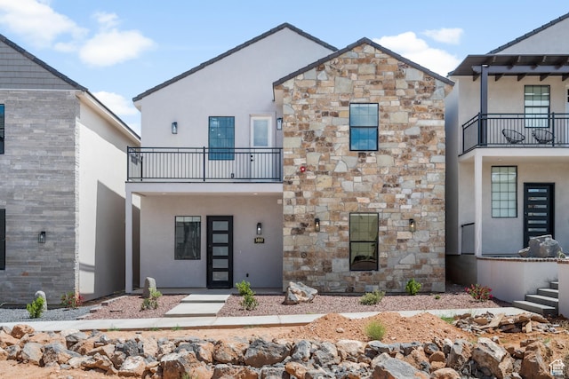 view of front facade with stone siding, a balcony, and stucco siding