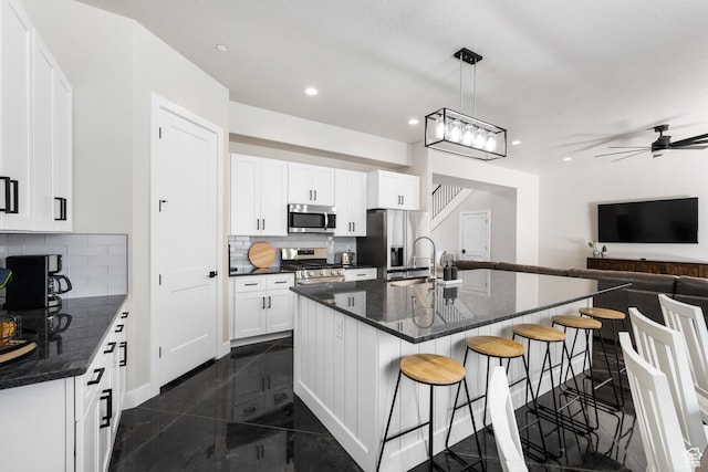kitchen with stainless steel appliances, a center island with sink, decorative light fixtures, and white cabinets