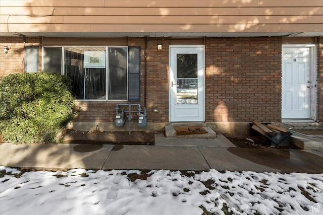 snow covered property entrance with brick siding