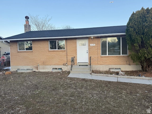 single story home featuring entry steps, a chimney, and brick siding