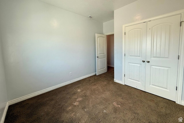 unfurnished bedroom featuring a closet, dark carpet, and baseboards
