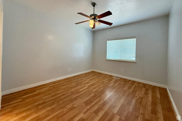 empty room featuring visible vents, baseboards, ceiling fan, light wood-style floors, and a textured ceiling
