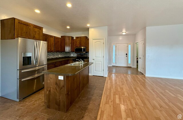 kitchen with an island with sink, a sink, dark countertops, stainless steel appliances, and dark wood-style flooring