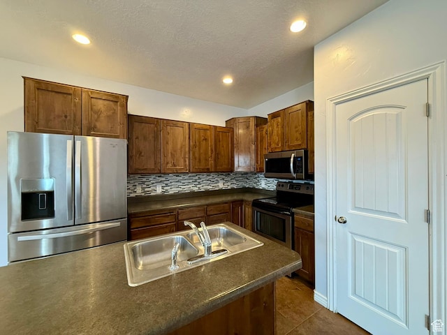 kitchen with dark countertops, a sink, decorative backsplash, appliances with stainless steel finishes, and dark tile patterned flooring