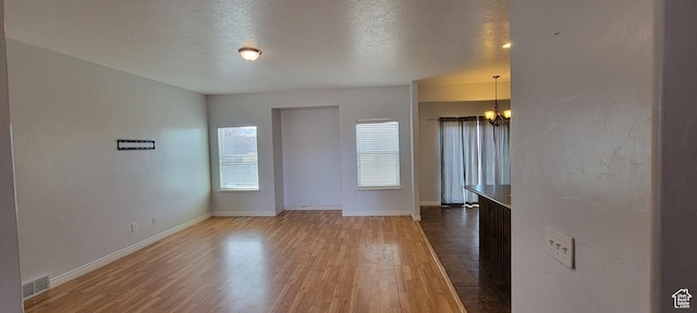 interior space featuring baseboards, a textured ceiling, an inviting chandelier, and wood finished floors