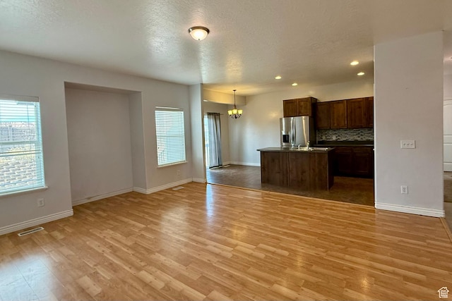 kitchen with visible vents, light wood-style flooring, backsplash, open floor plan, and stainless steel fridge with ice dispenser