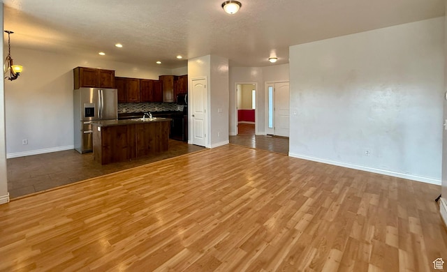 kitchen featuring black microwave, open floor plan, light wood-style flooring, stainless steel refrigerator with ice dispenser, and a sink