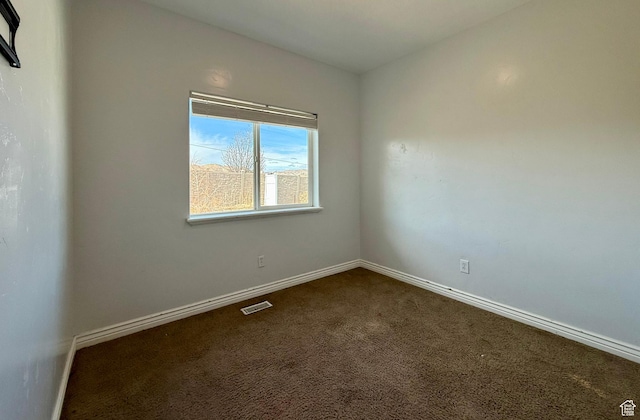 spare room featuring dark colored carpet, visible vents, and baseboards