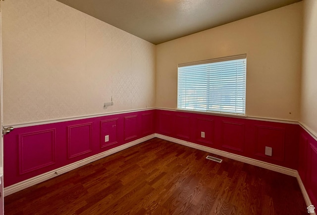 spare room with a wainscoted wall, visible vents, and wood finished floors