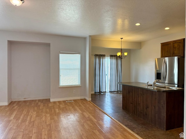 kitchen with stainless steel refrigerator with ice dispenser, a sink, dark countertops, wood finished floors, and a chandelier