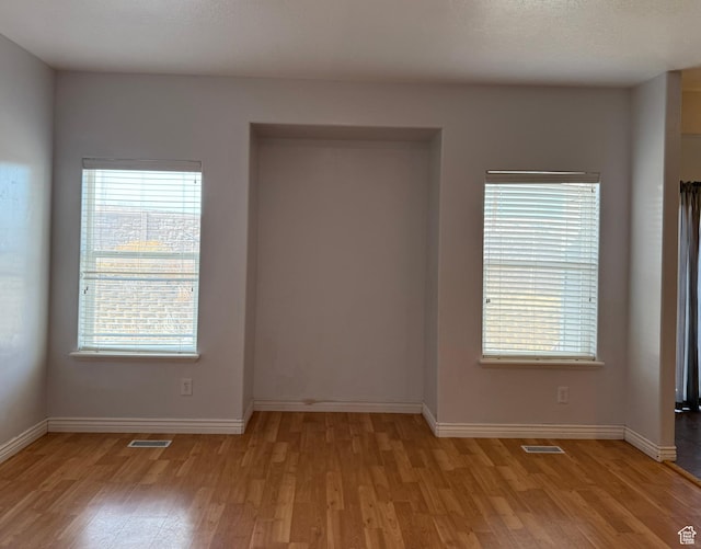 unfurnished room featuring light wood-type flooring, visible vents, and baseboards